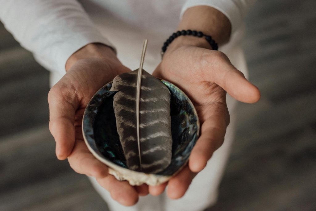 About Close-up of hands cradling a feather in a decorative bowl, symbolizing tranquility.