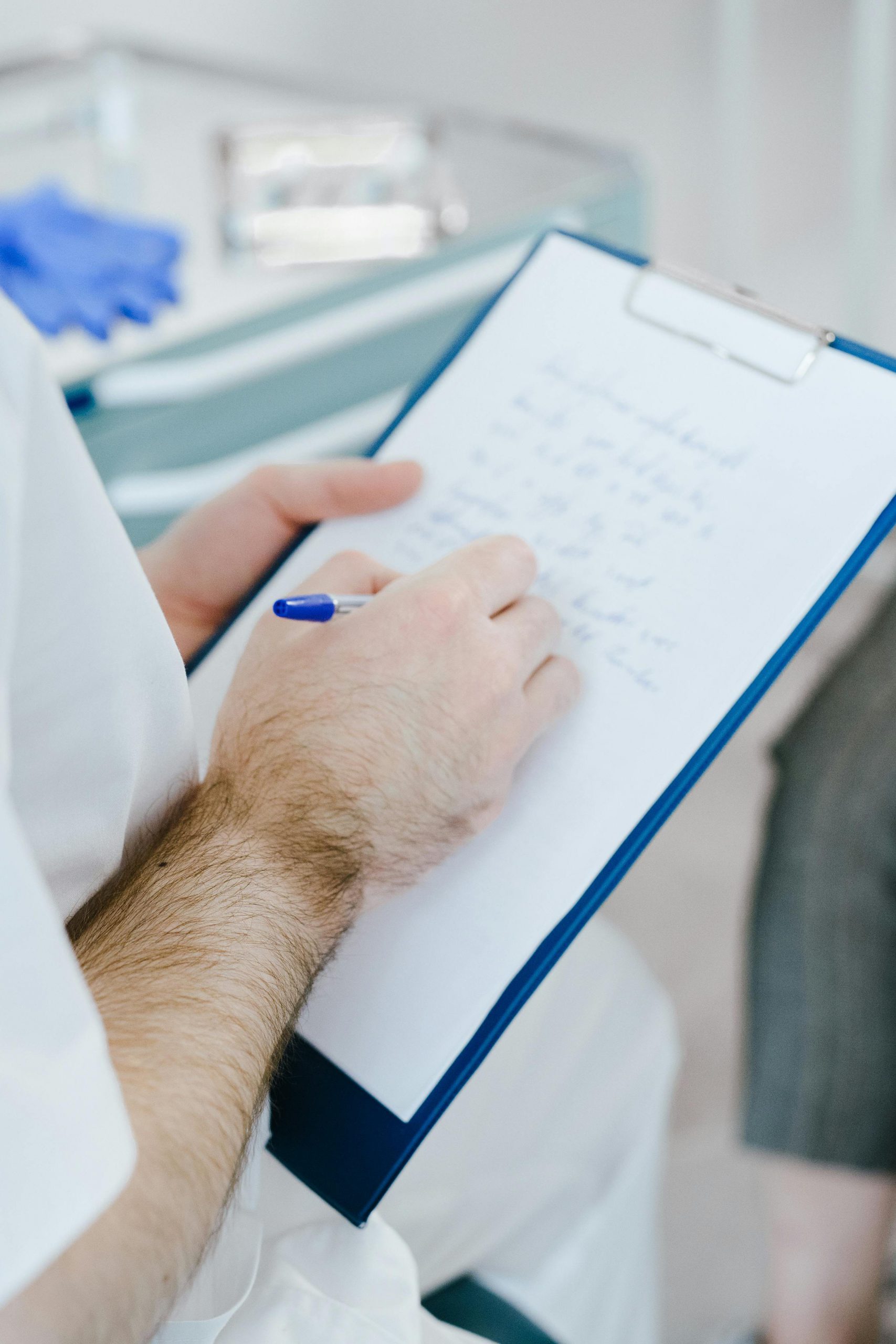 Medical professional writing patient notes on clipboard during consultation.